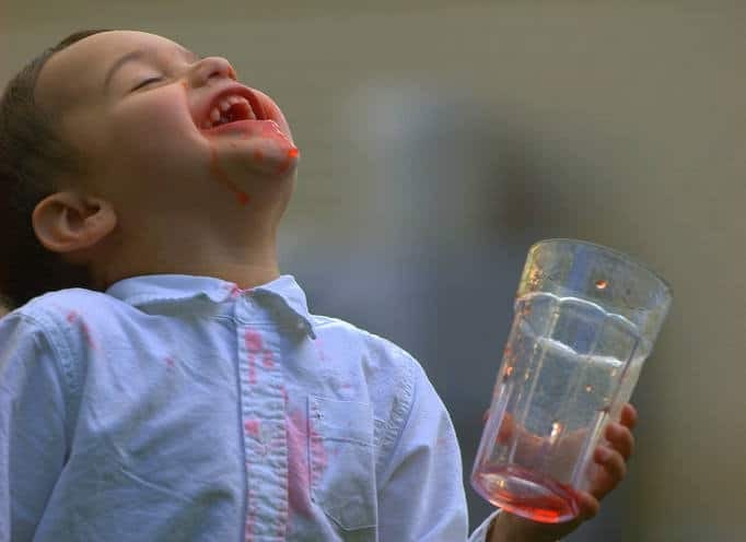 little boy with glass of Kool-Aid, red stain on shirt, messy face