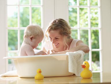 A baby taking a restful bath in a bathtub with a cheerful mother right beside