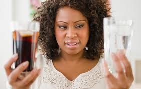 Fluoride: Not About Kid’s Teeth, About Ditching Hazardous Waste for Profit. A woman looking at her glass of water and also holding a glass of coke.